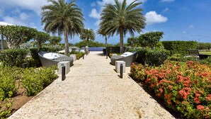 A pathway leading to a seating area with palm trees, a pool, and a landscaped garden. - Brand New Apartment, Panoramic Ocean Views (Noord)