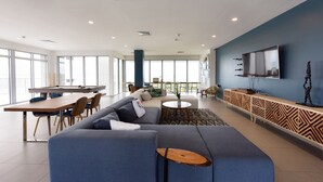 A modern living room with a blue sofa, a pool table, and a TV mounted on the wall. - Brand New Apartment, Panoramic Ocean Views (Noord)