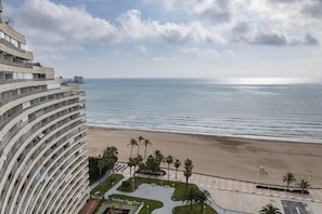 Un hotel frente al mar con una edificación curva, una playa arenosa y palmeras.