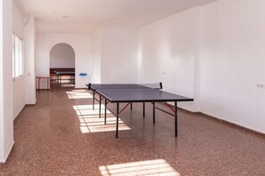 Un couloir avec des tables de ping-pong, une chaise rouge et un mur blanc orné d’une enseigne bleue.