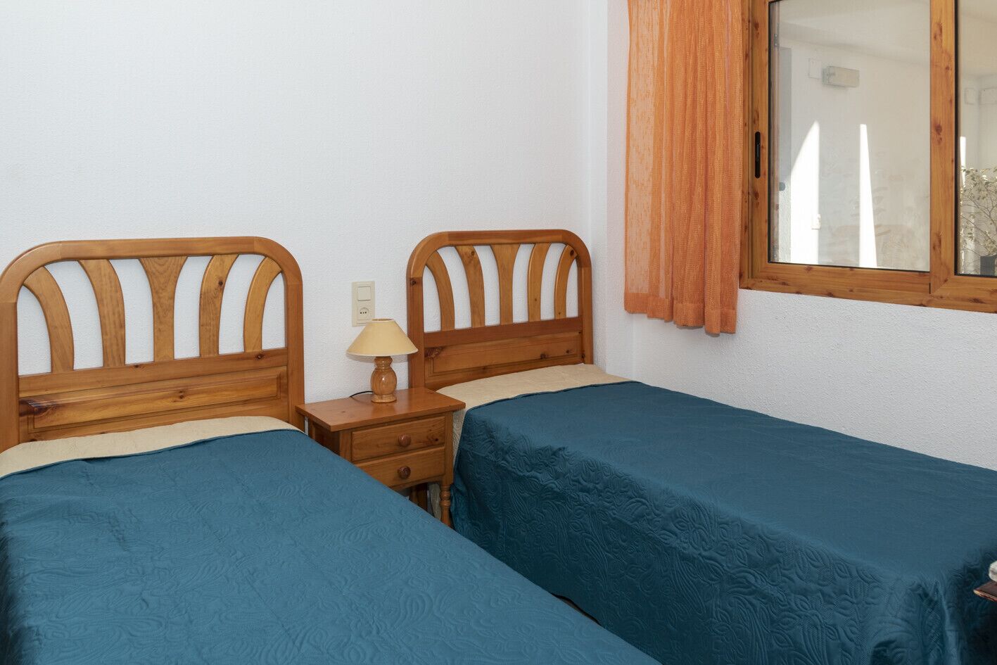 Una habitación con dos camas individuales, una mesita de noche con lámpara y una ventana con cortinas.