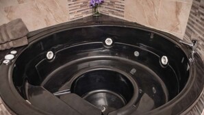 Una bañera de hidromasaje negra con desagüe central, frente a una pared de mármol.