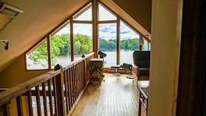 A wooden deck with a view of a lake, a chair, and a table. - Luxury Lakefront: Hot Tub, Fireplace, Pet Friendly, Arcade, Watercraft, + more! (Lake Ariel)