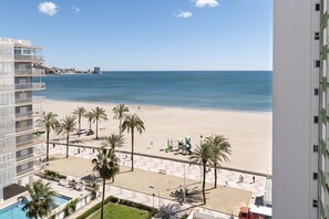 Um hotel na praia com piscina, palmeiras e vista para o mar.