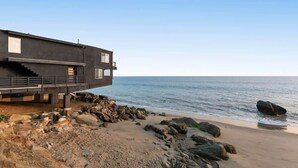 Une maison côtière moderne dotée d’un toit plat, de grandes fenêtres et d’un balcon donnant sur la plage.