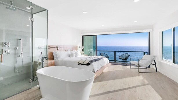 Une chambre moderne avec un grand lit, une douche en verre et une vue sur l’océan.
