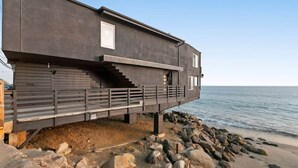 Une maison côtière moderne dotée d’un balcon, construite sur un littoral rocheux.