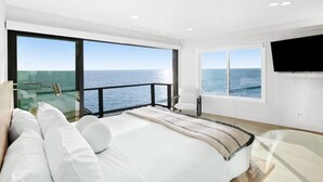 Une chambre moderne avec un grand lit, un téléviseur fixé au mur et un balcon offrant une vue sur la mer.