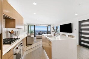 A modern kitchen with a central island, a dining area with a view, and a flat-screen TV mounted on the wall.