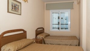 A room with two wooden beds, a small bedside table, a window with a view, and a wall-mounted picture. - MAR Y MONTAÑA, 2º-18 (Cullera)