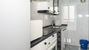 A compact kitchen with white cabinets, a built-in stove, a sink, and a window. - MAR Y MONTAÑA, 2º-18 (Cullera)