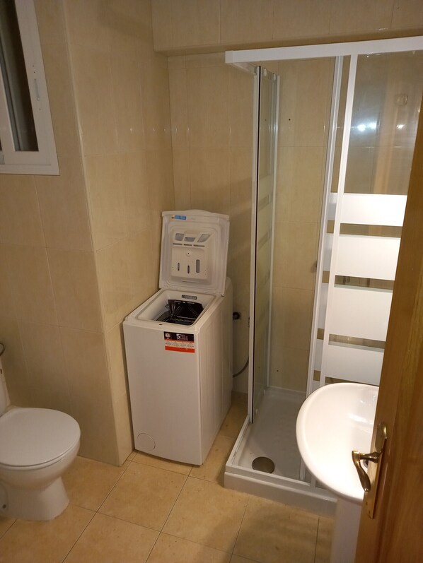 Une petite salle de bain comprenant des toilettes, un lave-linge et un espace douche.