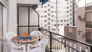 A balcony with a round table and four white chairs, a small sign with a house symbol, and a view of adjacent buildings. - MARI CARMEN, 2º-8 (Cullera)
