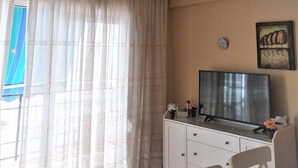 A room with a ceiling fan, a TV on a white cabinet, a window with sheer curtains, and a wall-mounted picture. - MARI CARMEN, 2º-8 (Cullera)