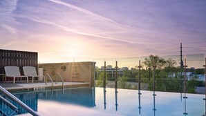 An infinity pool with clear water reflecting the sky, a set of white lounge chairs, and a warning sign on a wall. - Element by Marriott Nashville Vanderbilt West End (Nashville)
