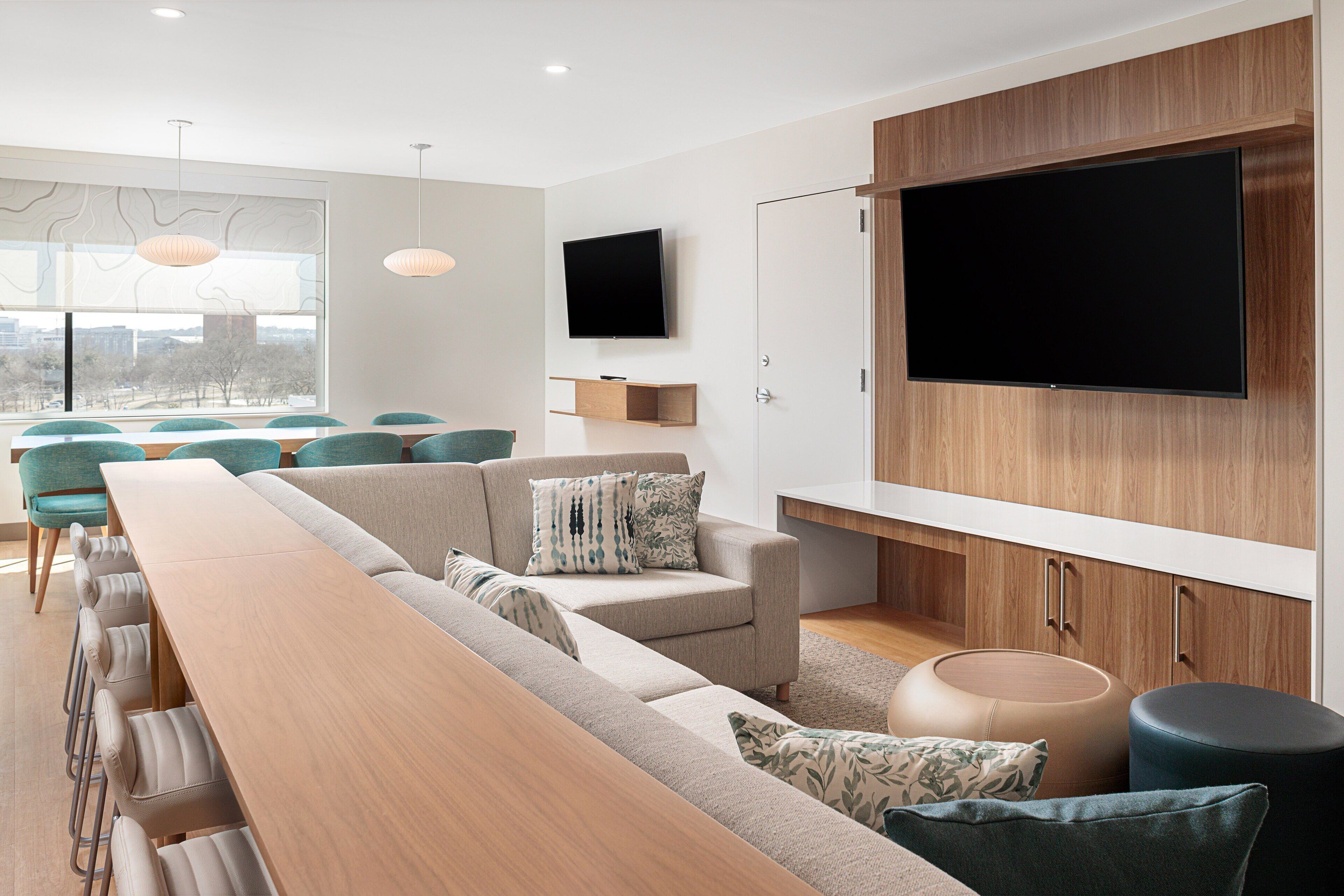 A modern living room with a long wooden table, a sofa, and a television mounted on the wall.