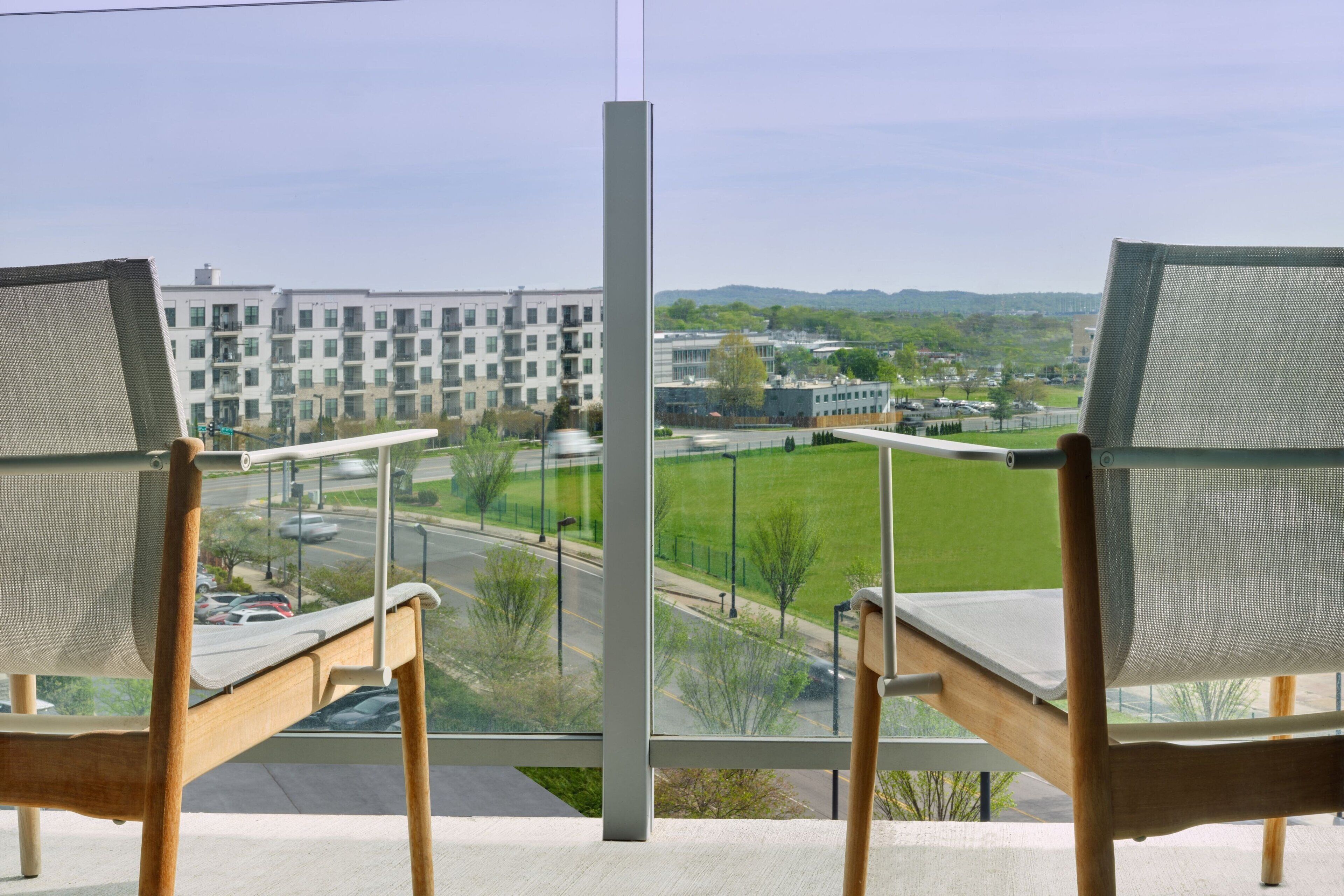 A view from a balcony with two chairs facing a road and a building complex.