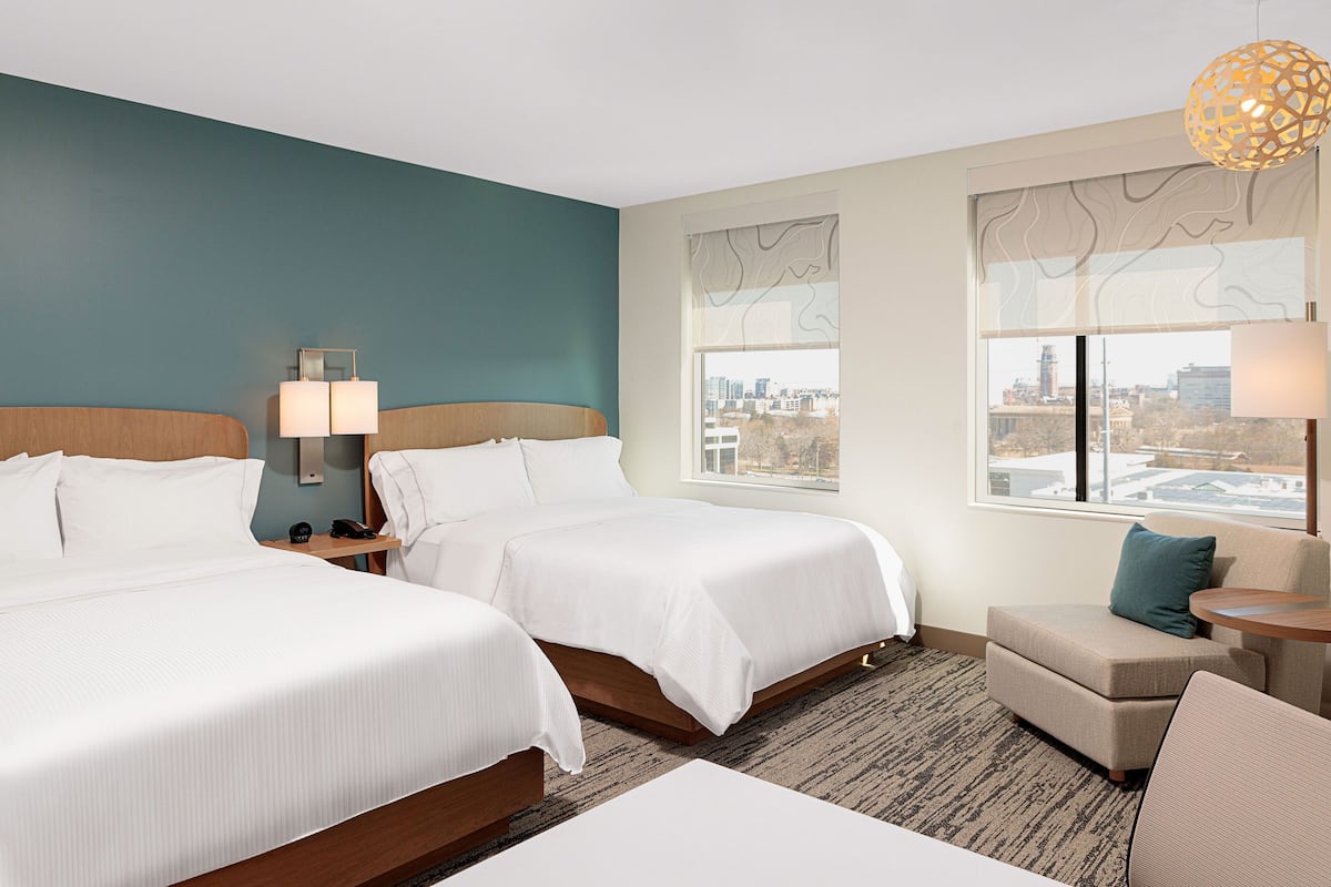 Een hotelkamer met twee bedden, een bank, een tafeltje en een raam met uitzicht op de stad.