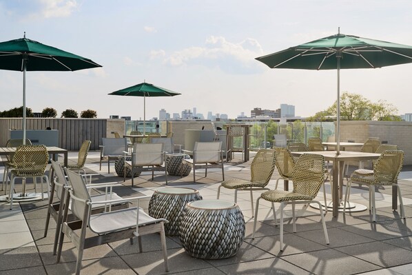 An outdoor patio with wicker furniture, round tables, and green umbrellas.
