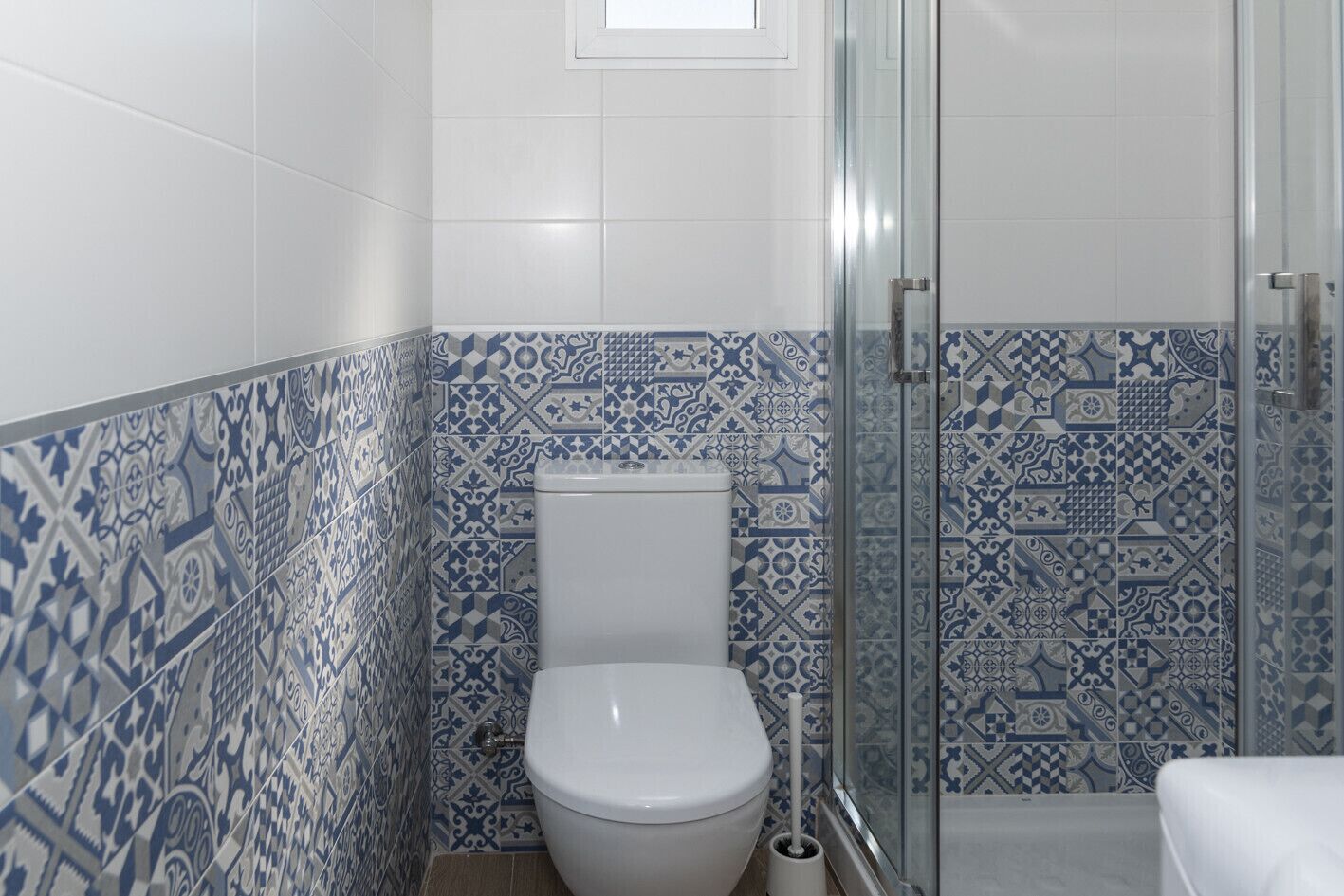 A bathroom with a white toilet, a glass shower enclosure, and patterned blue and white tiles.