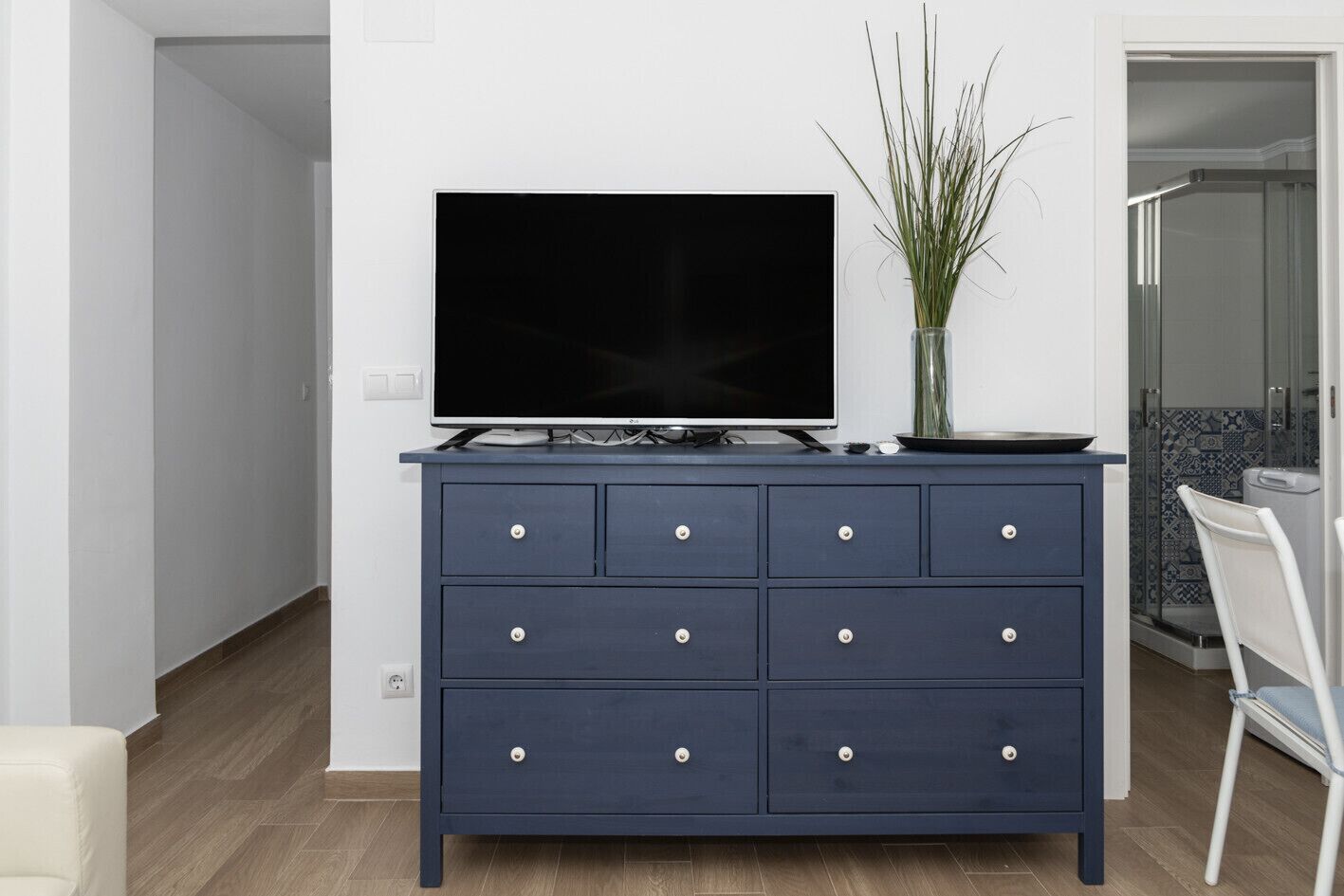 A modern living room with a dark blue dresser, a flat-screen TV, and a vase with green plants.