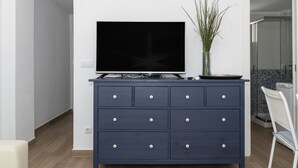 Een moderne woonkamer met een donkerblauwe dressoir, een flatscreen-televisie en een vaas met groene planten.