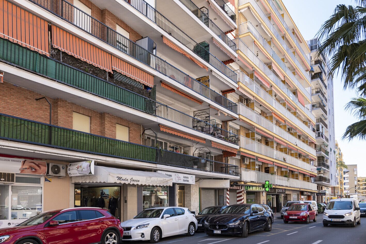 A multi-story building with balconies, a pharmacy, and various shops on the ground floor.