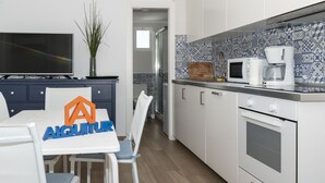 Een moderne keuken met witte kasten, een magnetron en een koffiezetapparaat. Er staat een eettafel met stoelen en een logo op de tafel.