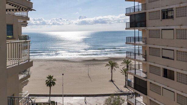 A beachfront hotel with balconies overlooking the ocean, palm trees, and a clear sky. - EL RACO, C-8º-16 (Cullera)