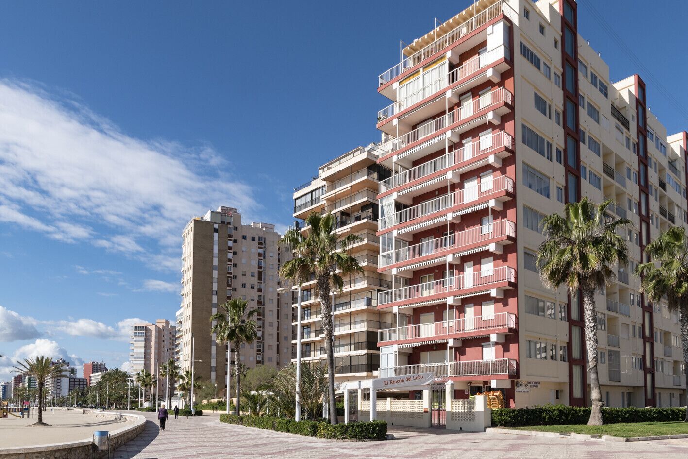 Un hotel de varios pisos con balcones, palmeras y un cielo despejado.
