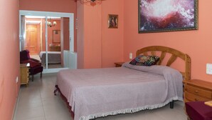 Un dormitorio con cama, mesita de noche, cómoda, silla y puerta que da a otra habitación.
