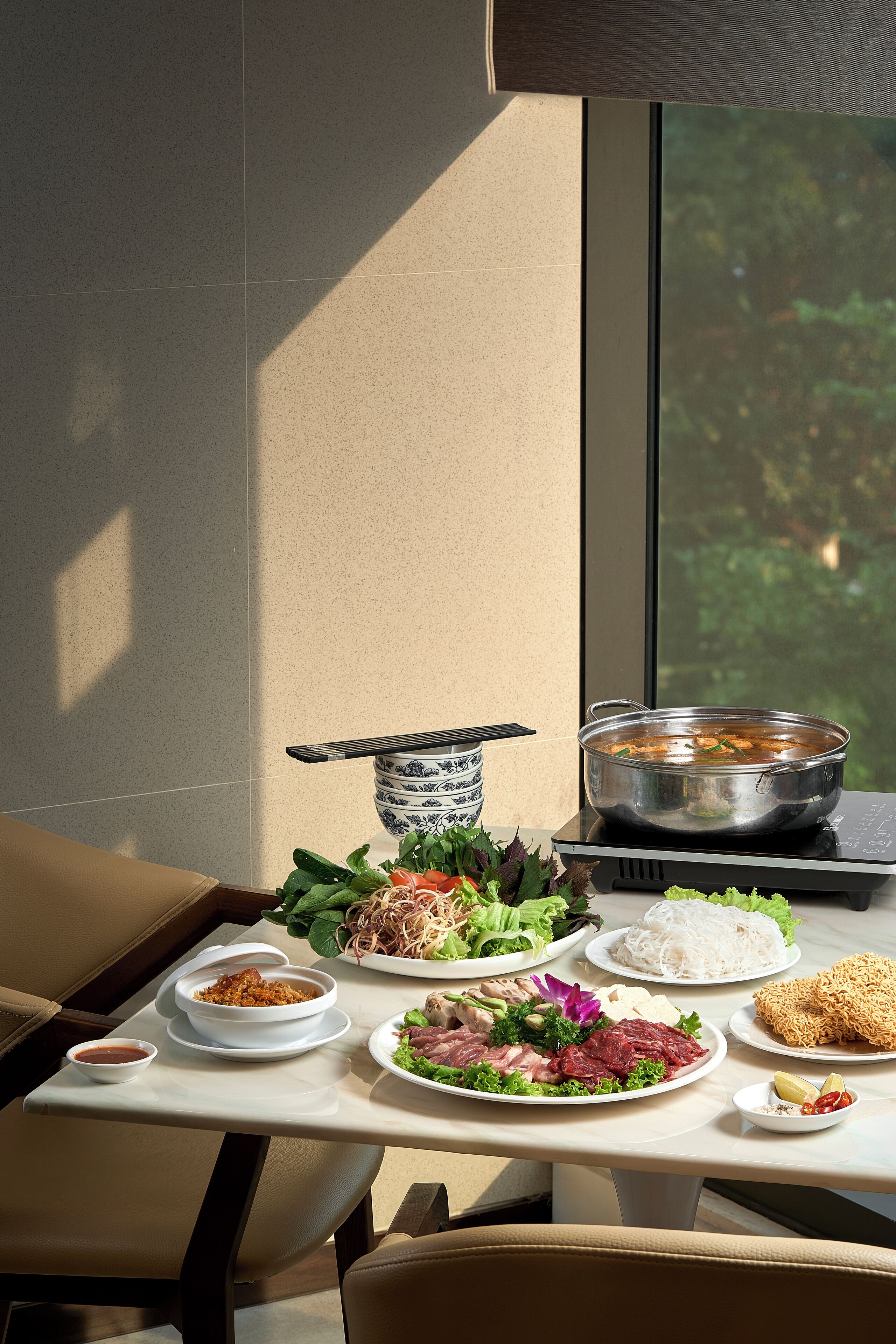 A dining table with various dishes, a bowl of soup, and a window with a view of greenery.