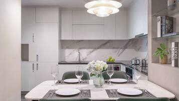 A modern dining area with a marble countertop, white cabinets, and a glass shelf with books and a plant.