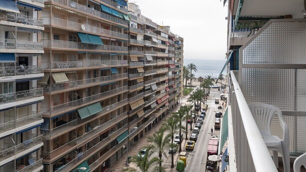 Ein mehrstöckiges Hotel mit Balkonen, eine Straße mit Palmen und Blick aufs Meer.