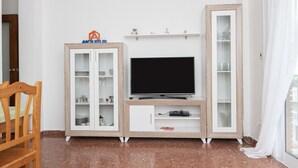 Ein Wohnzimmer mit Fernseher auf einem Holzboden, einer Vitrine und einem Sessel.