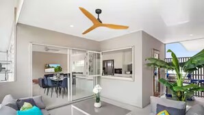 Ein modernes Wohnzimmer mit Deckenventilator, Essbereich mit Tisch und Stühlen sowie ein großes Fenster mit Aussicht.