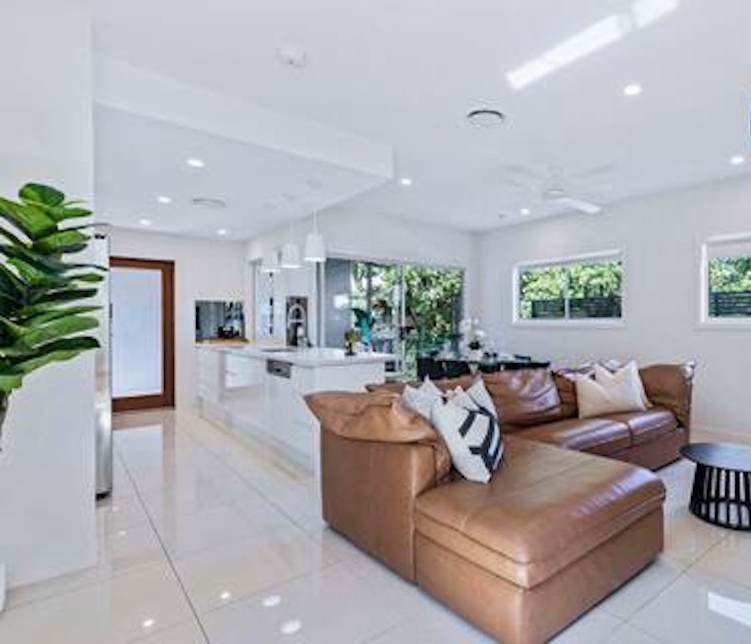 A modern living room with a brown leather sofa, a small round table, and a kitchen area in the background.