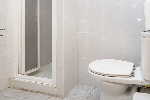 Une salle de bain comprenant des toilettes, une douche avec une porte en verre et des murs carrelés.