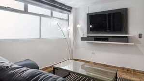 Una sala de estar moderna con un televisor de pantalla plana montado en la pared, una mesa de centro de vidrio y un sofá de cuero.