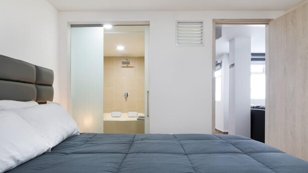 Habitación de hotel moderna con una cama grande, baño con ducha y vistas al exterior.