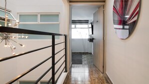 Un pasillo con una lámpara moderna, barandilla de metal y un cuadro abstracto grande en la pared.