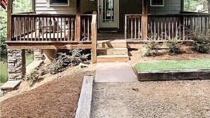 Una casa a due piani in legno con un portico, un camino e un piccolo giardino antistante.