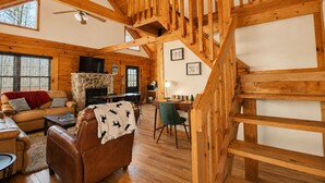 Un interior de madera con una escalera, una chimenea de piedra, un sofá y una televisión.