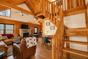Un intérieur en bois avec un escalier, une cheminée en pierre, un canapé et un téléviseur.