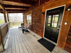 A wooden cabin with a porch, a black door, and two Adirondack chairs.