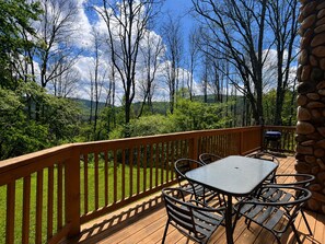 A deck with a table and chairs, surrounded by a wooden railing, overlooking a forested landscape. - 11 Beech - Cozy, Pet-Friendly Cabin! (Slaty Fork)