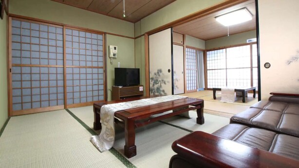A traditional Japanese room with tatami flooring, a low wooden table, a sofa, sliding doors, and a television. - Hikari no Yado - Detached house for rent in Anan City, Tokushima Prefecture (徳島県)