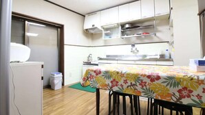 A compact kitchen with white cabinets, a small refrigerator, and a dining table with a floral tablecloth. - Hikari no Yado - Detached house for rent in Anan City, Tokushima Prefecture (徳島県)