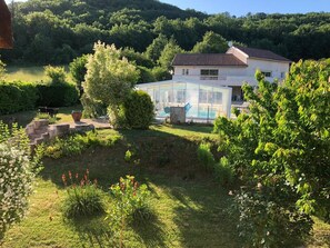Une maison dotée d’une piscine à laquelle on accède par une structure entièrement vitrée, entourée d’une végétation luxuriante et d’un jardin bien entretenu.