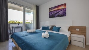 A bedroom with a large bed, a nightstand, a desk, and a view of a balcony. - Mare Room with Balcony and Shared Pool (Novalja)